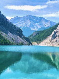 a lake surrounded by mountains and trees in the middle of it with clear blue water