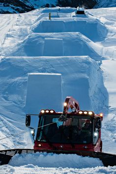 a snow plow is moving through the snow in front of a ski slope area