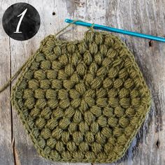 a green crocheted pot holder sitting on top of a wooden table next to a knitting needle