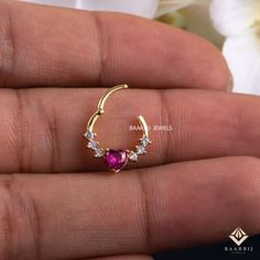 a woman's hand holding a gold nose ring with pink and white stones