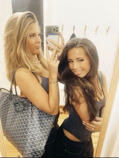 two beautiful young women standing next to each other in front of a mirror holding up their cell phones