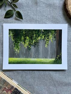 a card with an image of trees and grass on it, next to a piece of paper