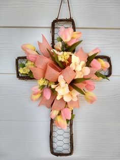 a cross hanging on the side of a building with pink and yellow flowers in it