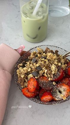 a bowl of strawberries and granola next to a cup of green smoothie