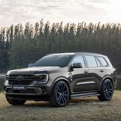 the new ford explorer is parked in front of some trees and grass with its lights on