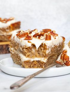 a piece of carrot cake on a plate with a fork next to it and another slice in the background