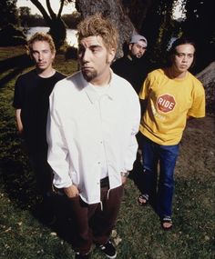 three men standing next to each other in front of a tree and grass area with one man looking at the camera