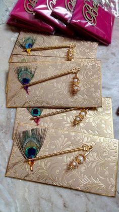 peacock feathers on gold embossed cards with pink envelopes next to bag of candy