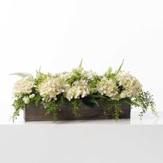 an arrangement of white flowers and greenery in a wooden box on a table against a white background