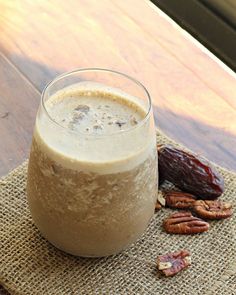 a glass filled with liquid sitting on top of a table next to pecans and dates