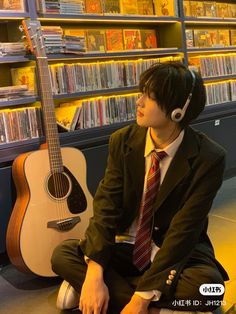 a man sitting on the floor with headphones in his ears next to a guitar