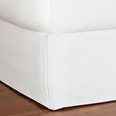 a bed with white sheets on top of it and wood flooring in the background