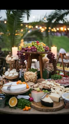 an assortment of cheeses, meats and fruits on a table with candles in the background