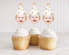 three cupcakes with white frosting and one has a birthday hat on top