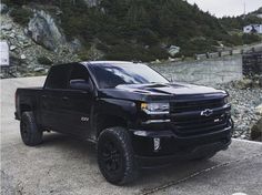 a black truck parked on top of a rock covered hillside next to a body of water