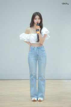 a woman standing in front of a white wall with her hands on her hips and holding a microphone