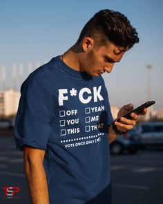 a man standing in a parking lot looking at his cell phone while wearing a f k t - shirt