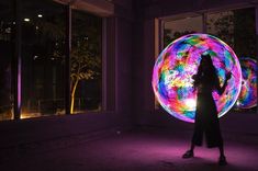 a woman is standing in front of a large ball with colorful lights on the inside