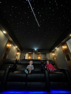 two children sitting in the middle of a movie theater with stars on the ceiling and blue lights