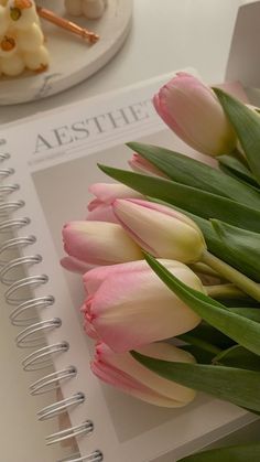 pink and white tulips sitting on top of a table next to a spiral notebook