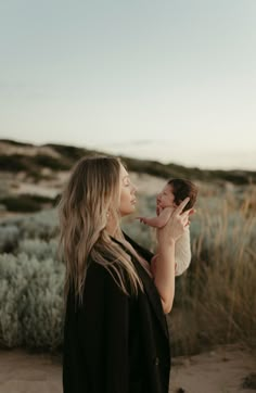 a woman holding a baby in her arms and looking at the sky while standing on a beach