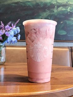 a pink drink sitting on top of a wooden table next to a vase with purple flowers