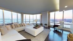 a living room filled with white furniture and large windows overlooking the cityscape in the distance