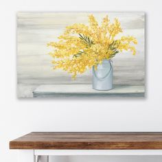 a painting of yellow flowers in a blue vase on a white wall above a wooden table