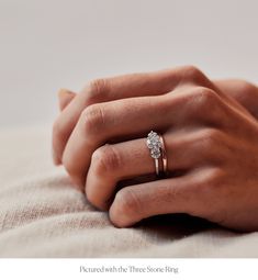 a woman's hand with a diamond ring on her left hand, resting on the bed