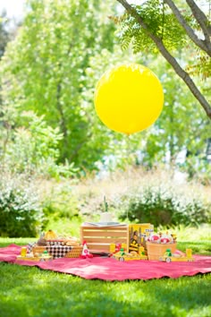 a yellow balloon is in the air above a picnic table with food and drinks on it