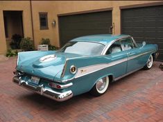 an old blue car parked in front of a garage with a cat on the sidewalk