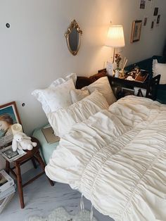 an unmade bed in a bedroom next to a table with pictures on the wall