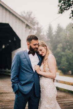 a bride and groom standing together in front of a covered bridge