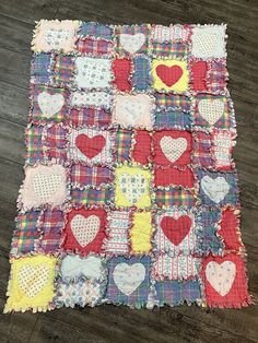 a patchwork quilt with hearts on it sitting on top of a wooden floor in front of a wall