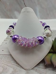 "Handmade by me-lilac glass crystal beads-lilac ceramic flower beads-various glass beads-fits a 7 1/4\" wrist-silver tone-lobster clasp-1\" extender chain-give to someone you know is a purple lover! Makes a statement when wearing!" Purple Beaded Bracelets With Watch, Purple Flower-shaped Beaded Bracelets, Purple Flower Shaped Beaded Bracelets, Lavender Beaded Bracelet Jewelry, Lavender Bracelets With Spacer Beads As Gift, Lavender Bracelets With Spacer Beads For Gift, Purple Beaded Flower Bracelets, Handmade Lavender Stretch Bracelet With Round Beads, Purple Flower Jewelry With Colorful Beads