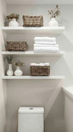 a white toilet sitting in a bathroom next to shelves filled with towels and vases