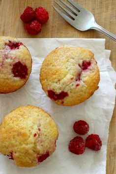 three raspberry muffins sitting on top of a piece of parchment paper