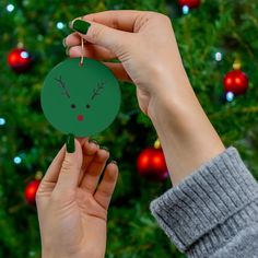 a person holding up a christmas ornament in front of a christmas tree