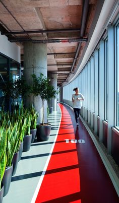 a woman is walking down the red carpeted walkway in an office building with large windows