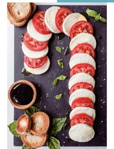 sliced tomatoes, mozzarella and basil on a black cutting board with bread in the background