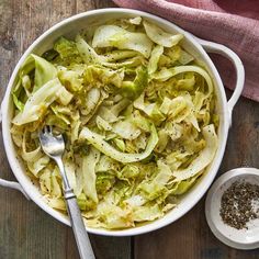 a white bowl filled with cabbage and some seasoning next to a pink towel on top of a wooden table