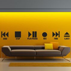 a couch sitting in front of a yellow wall with various signs on the wall behind it