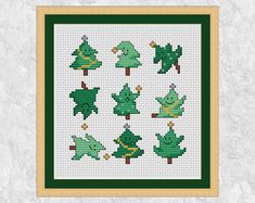 cross stitch christmas trees in green and gold framed on a white background with a wooden frame