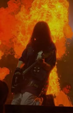 a man with long hair playing guitar in front of flames