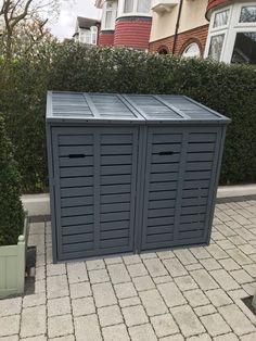 two blue storage containers sitting on top of a brick sidewalk next to bushes and trees