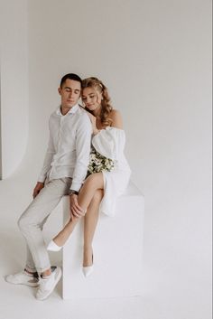 a young man and woman sitting on top of a white box posing for the camera