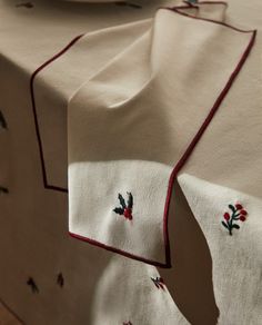 a white table cloth with red trim and embroidered holly designs on it, sitting on a wooden floor