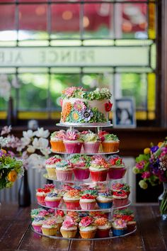 there are many cupcakes on the table and one is stacked high with flowers