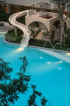 an outdoor swimming pool with a slide in the middle and trees around it at night