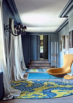 a living room with blue walls and yellow chair in the center, rug on the floor